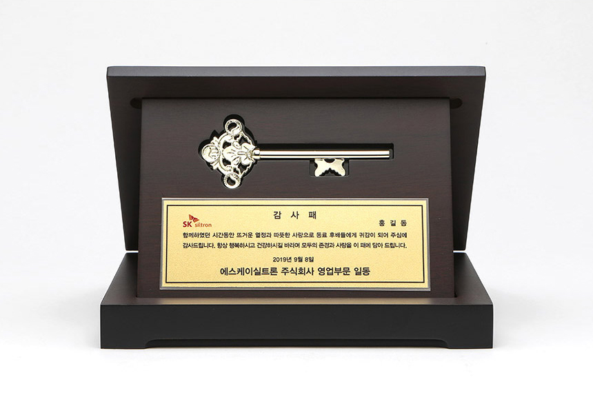 모형 열쇠와 금박 명판이 세련되게 배치된 골드플레이트 상패 클로즈업 이미지